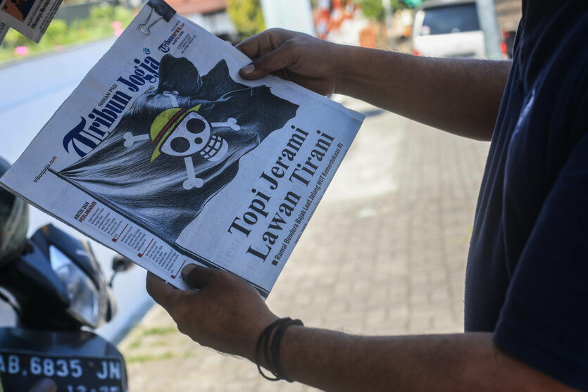Eine Person zeigt eine Tageszeitung mit One Piece-Illustration