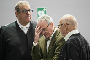 Drei Männer stehen nebeneinander. Einer fässt sich an den Kopf