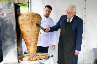 Ein Mann schneidet von einem Dönerspieß Fleisch ab. Ein anderer Mann schaut dabei zu