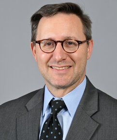 Ein weißer Mann mit Brille, Anzug und Krawatte