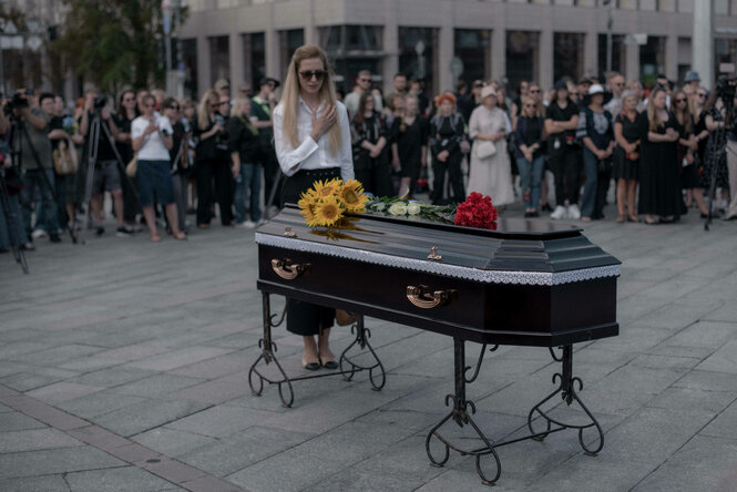 Eine Frau steht an einem schwarzen Sarg auf einem Platz