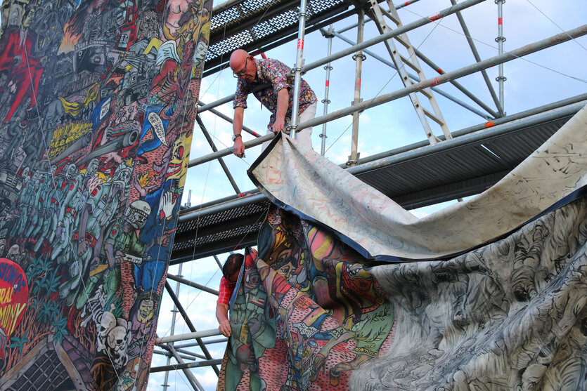Männer auf einem Gerüst hängen ein Kunstwerk ab