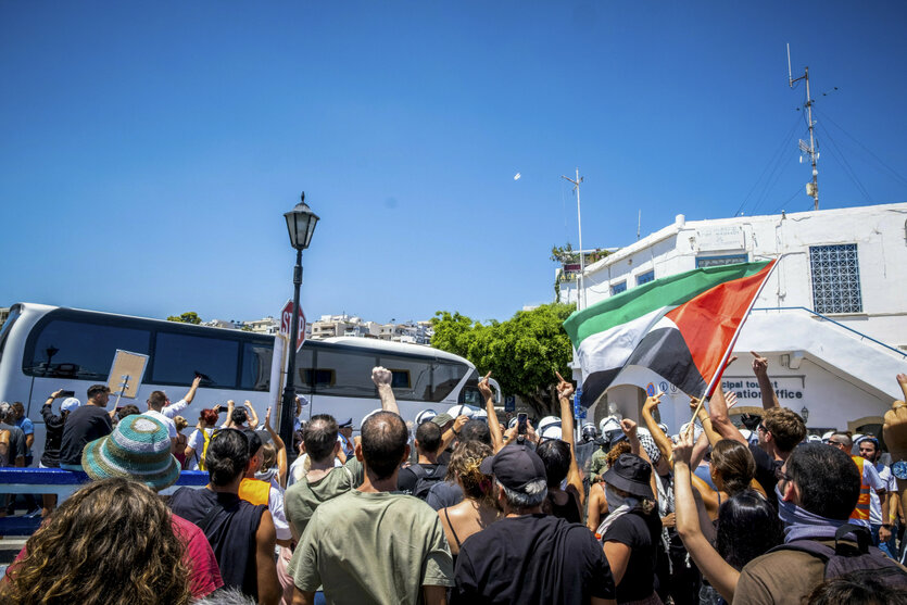Gruppe protestierender Menschen, einige mit erhobenen Mittelfingern, vor einem Schiff