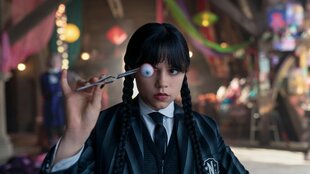 Jenna Ortega, mit schwarzen Zöpfen, hält ein Auge mit Pincetten