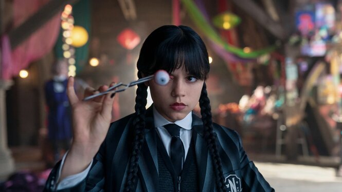 Jenna Ortega, mit schwarzen Zöpfen, hält ein Auge mit Pincetten