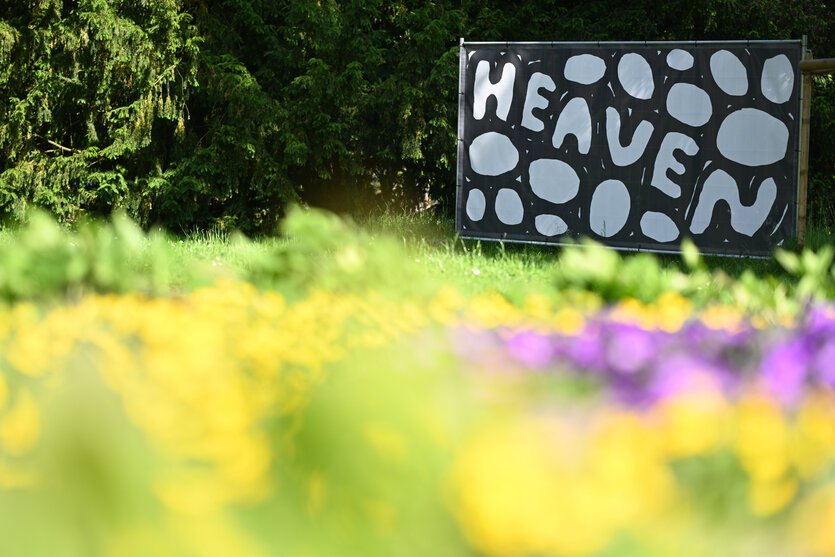 Eine Wiese im Schloßgarten. Auf ihr steht ein Bauzaun mit einer Arbeit von Stefan Marx: diese zeigt das Wort "Heaven"
