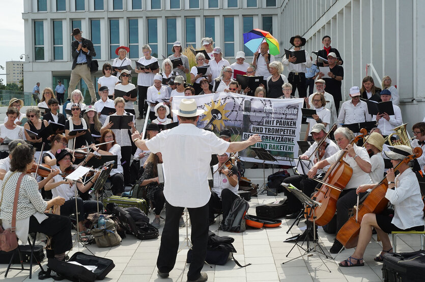 Vor einem Bürogebäude tritt ein Orchester auf, alle sind in weiß gekleidet