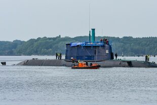 Ein U-Boot schwimmt in der Kieler Förder, Männer stehen oben auf dem Boot und ein kleines Schiff fährt nebenher
