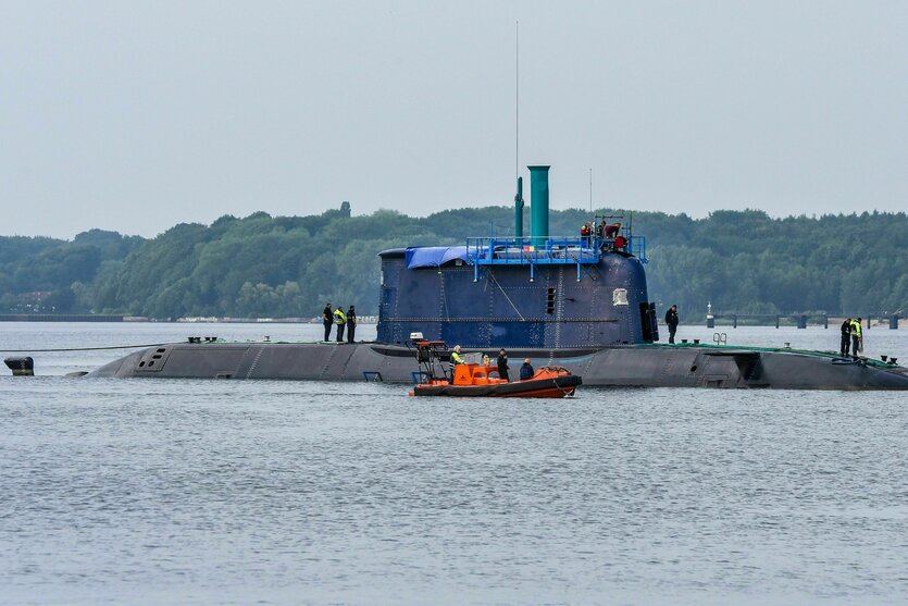 Ein U-Boot schwimmt in der Kieler Förder, Männer stehen oben auf dem Boot und ein kleines Schiff fährt nebenher