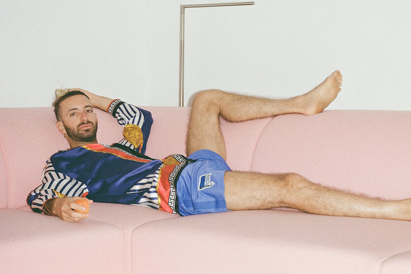 Der Maler Navot Miller liegt lasziv auf einem eckigen rosa Sofa