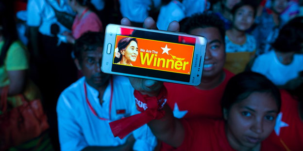 Ein blau angeleuchteter Mensch hebt ein Smartphone mit der Display „We are the winner“ hoch