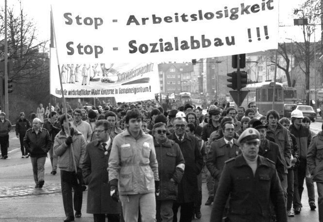 Protestaktion in Wtten, die Protestierenden, vor allem Männer in Mänteln gehen hinter einem Transparent mit der Losung: Stop Sozialabbau !! Stopp Arbeitslosigkeit !