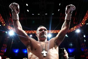 Weltmeister im Schwergewicht. Ein Boxer mit naktem Oberkörper reckt beide Arme in die Höhe, er trägt Boxhandschuhe