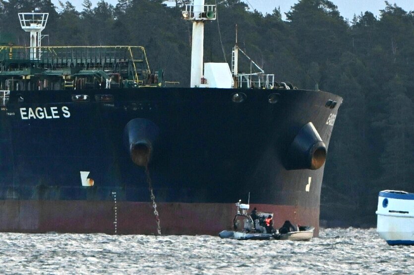 Das Schiff Eagle S schwimmt auf dem Wasser, ein kleines Boot befindet sich am Bug und das Ufer ist bewaldet