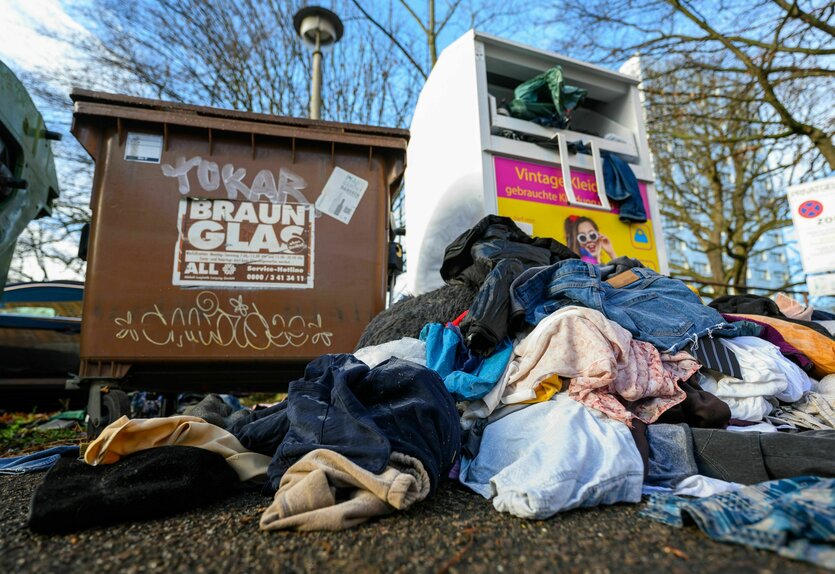 Kleidermüll vor einem Sammelcontainer