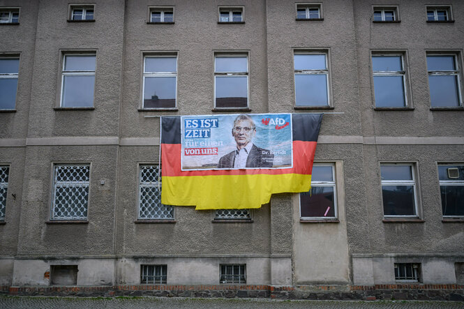 Ein älteres Wahlplakat von Hans-Christoph Berndt, Vorsitzender der Brandenburger AfD-Fraktion, hängt auf einer Deutschlandflagge an einer tristen Hausfassade