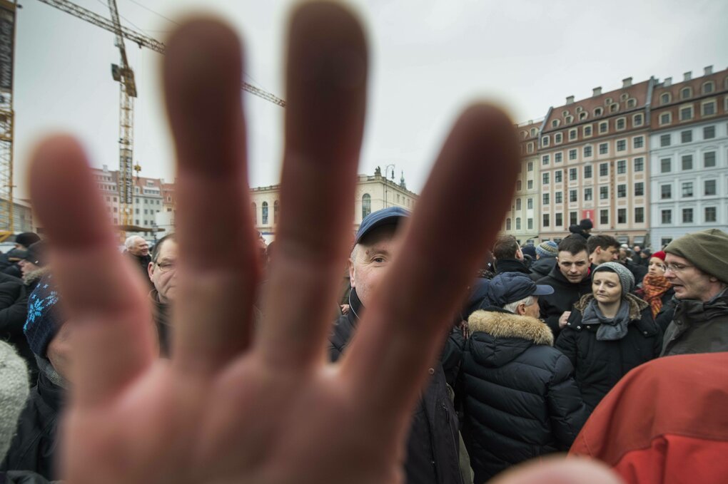 Protest, eine Person greift direkt in die Kamera, alles ist graue, die Menschen scheinen depressiv