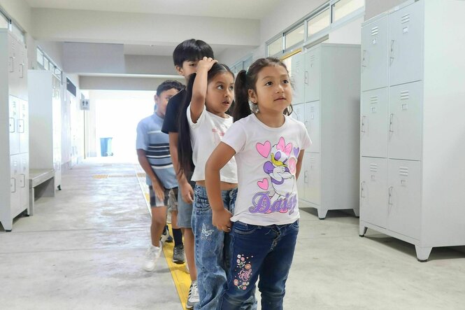 Kinder stehen auf einer gelben Linie hintereinander in einer Schlange