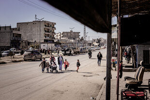 Eine Gruppe Kinder begleitet von zwei weiblich gelesenen Personen überqueren eine Straße in Kobane in Nordsyrien