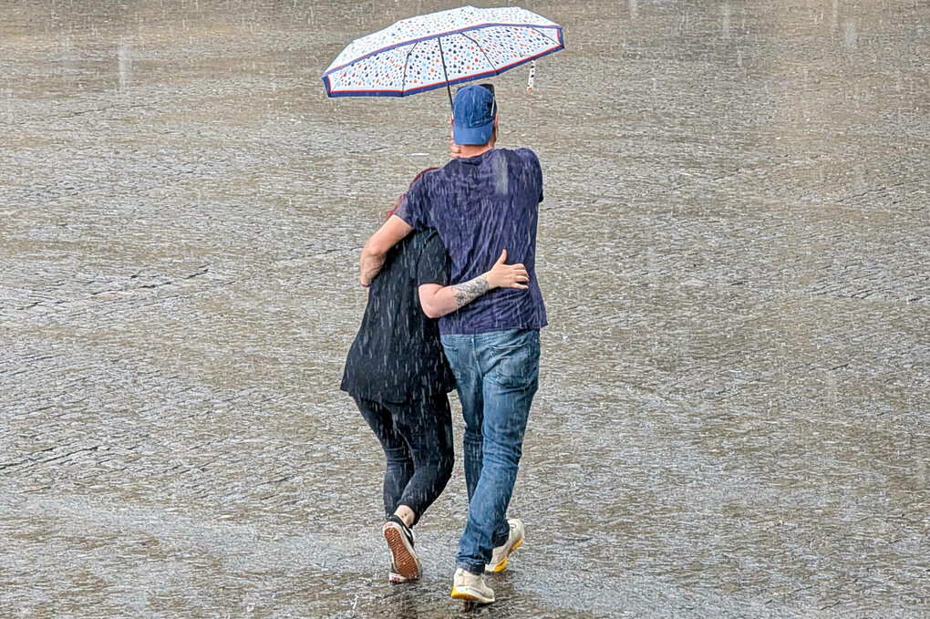 Paar läuft unter einem Regenschirm durch starken Regen