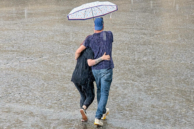 Paar läuft unter einem Regenschirm durch starken Regen