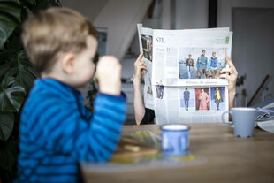 Symbolfoto: Ein Vater liest in einer Zeitung während sein Kind am Tisch alleine isst