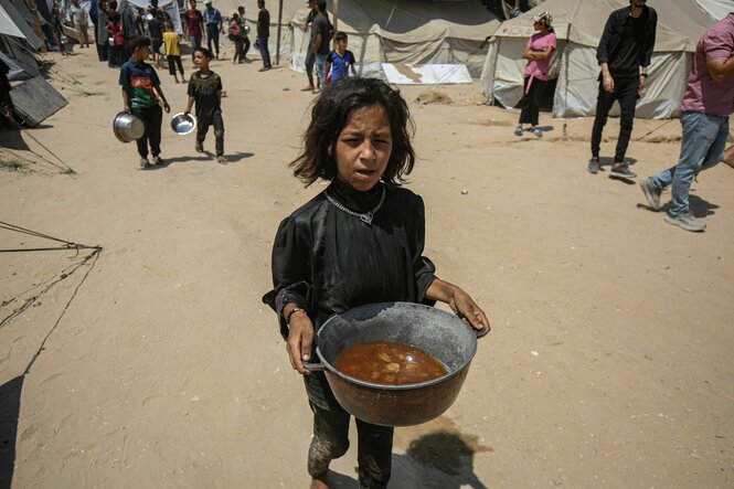 Ein junges Mädchen mit halbleerem Topf in Händen, in Mitten der Ruinenlandschaft von Gaza
