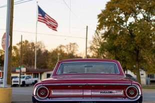 ein roter Ford aus dem Jahr 1964 steht auf einem Platz, eine US-Flagge weht im Hintergrund