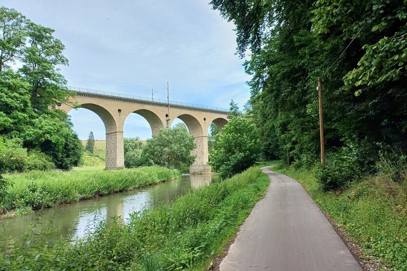Eine Brücke an einem Gewässer, daneben ein Radweg.