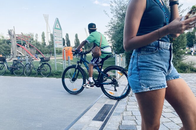 Ein Radfahrer und eine Fußgängerin über der Grenzmarkierung im Mauerpark