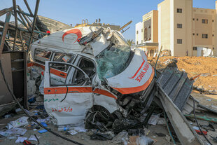 Ein ausgebombter Rettungswagen mit arabischen Schriftzeichen vor einer Ruine