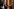 Helmut Schmidt mit Zigarette sitzt auf einem Stuhl, neben ihm steht eine Blume