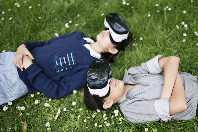 zwei Kinder liegen mit VR Brillen auf einer Wiese