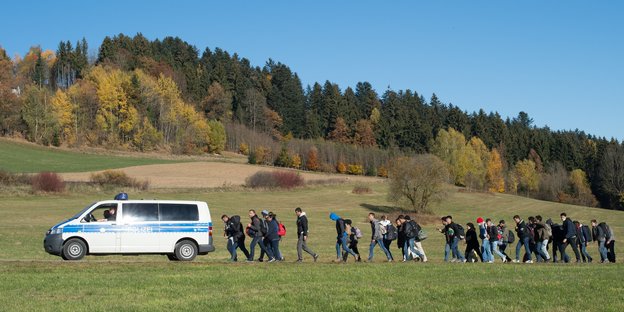 Flüchtlinge gehen am 01.11.2015 nahe Wegscheid (Bayern) nach der Überquerung der Grenze von Österreich nach Deutschland hinter einem Polizeifahrzeug zu einer Aufnahmestation.