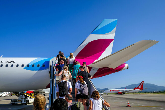 Am Flughafen Korfu steigen Urlauber ueber eine Aussentreppe auf dem Vorfeld in ein Eurowings Flugzeug