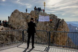 Ein Mann fotografiert Protestierende beim EU-Migrationsgipfel auf der Zugspitze im Juli 2025
