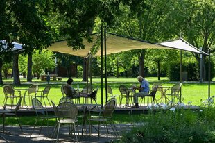 Bei Temperaturen von fast 30 Grad sitzen eine Frau und ein Mann unter einem Sonnensegel zur Abkühlung im Stadtpark