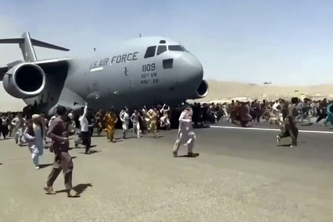 Screenshot; Hunderte von Menschen laufen neben einem Transportflugzeug vom Typ C-17 der US-Luftwaffe her, während es auf der Startbahn des internationalen Flughafens in Kabul rollt.