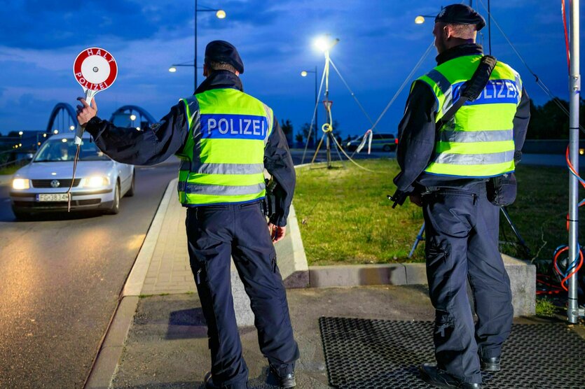 zwei Polizisten stehen nachts am Straßenrand und halten ein Stop Schild hoch