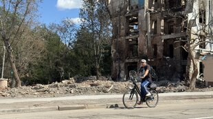 Ein Mann fährt auf einem Fahrrad an einem zerstörten Haus vorbei