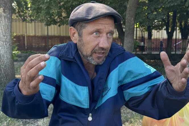 Ein Mann in blauer Sportjacke und mit Schiebermütze spricht und gestikuliert dabei mit seinen Händen