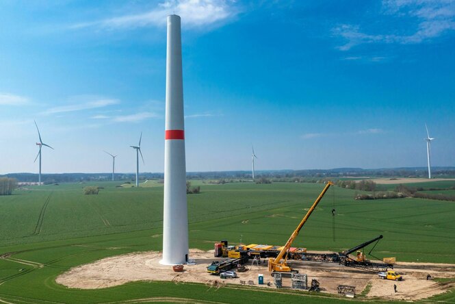 Windrad im Aufbau vor blauem Himmel, der Turm steht schon, der Rotor liegt auf dem Boden
