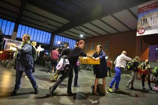 Menschen bilden im Bahnhof München eine Kette, um Kisten mit Lebensmitteln weiter zu reichen, dabei haben sie gute Laune