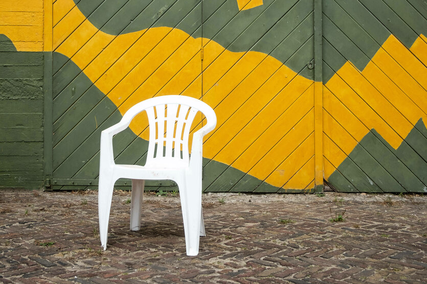 Eine weißer Plastikstuhl steht vor einem farbigen Tor