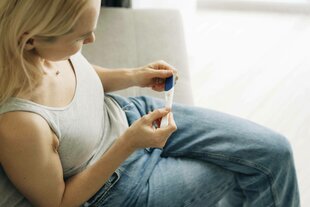 Eine Frau hält einen Schwangerschaftstest in den Händen und wartet auf das Ergebnis