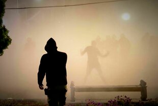 Mann in einer Kapuzenjacke steht vor hell erleuchteten Rauchschwaden