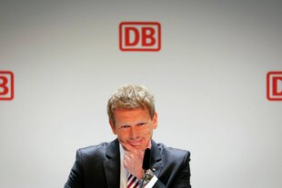 Richard Lutz vor weiser Wand mit roten DB Logos, zweifelend lächelnd nach unten blickend