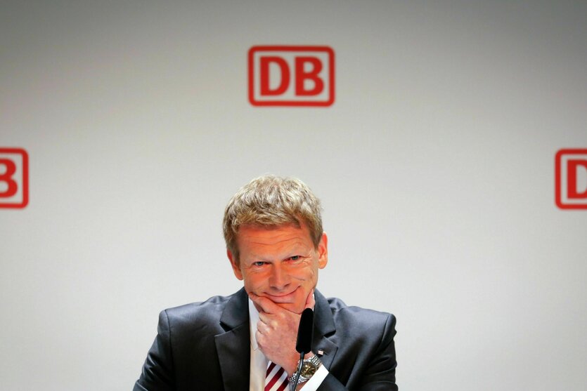 Richard Lutz vor weiser Wand mit roten DB Logos, zweifelend lächelnd nach unten blickend