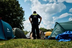 Ein Polizist steht in einem Protestcamp, die Hände in die Hüfte gestützt