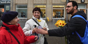 Ein Mann verschenkt gelbe Blumen an zwei Frauen